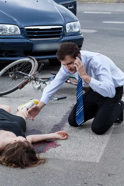 Motor Vehicle Accidents 4 A man talking on a phone to the ambulance after crashing into a woman on a bicycle.
